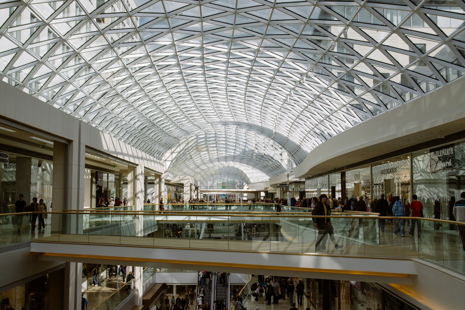 Shoppers walking through a bright modern retail concourse, representing enterprise omnichannel commerce across brands and markets